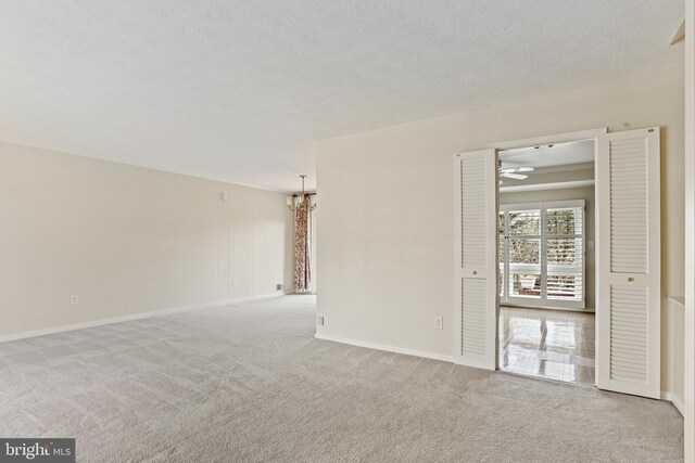 unfurnished room featuring light carpet, ceiling fan with notable chandelier, a textured ceiling, and baseboards