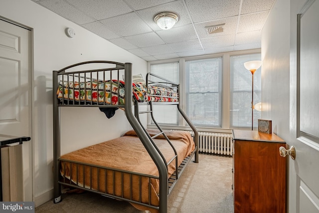 bedroom with radiator heating unit, a drop ceiling, carpet flooring, and visible vents