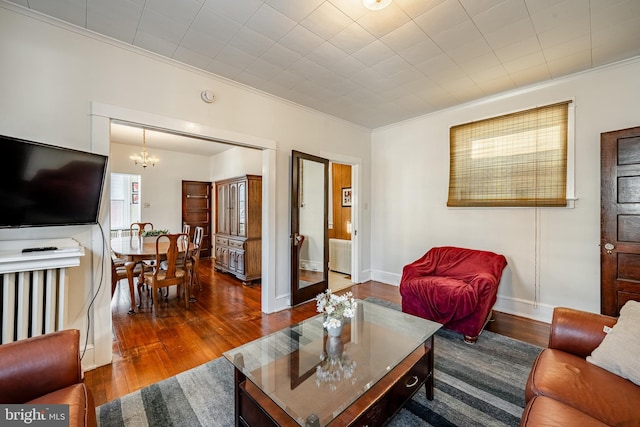 living area featuring dark wood-style floors, ornamental molding, baseboards, and an inviting chandelier