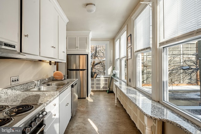 kitchen with light stone counters, range hood, stainless steel appliances, white cabinetry, and a sink