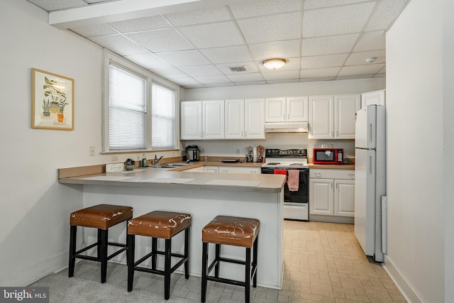 kitchen with electric stove, a peninsula, freestanding refrigerator, and white cabinetry