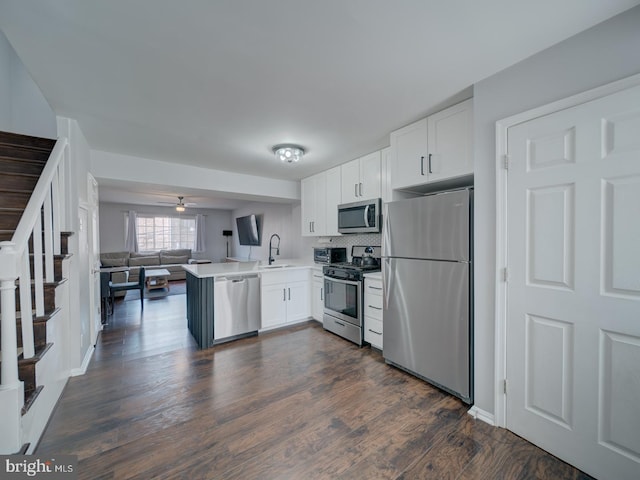 kitchen featuring a peninsula, a sink, white cabinetry, open floor plan, and appliances with stainless steel finishes