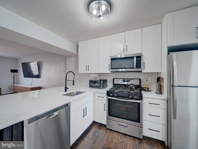 kitchen featuring light stone counters, stainless steel appliances, a sink, white cabinetry, and backsplash