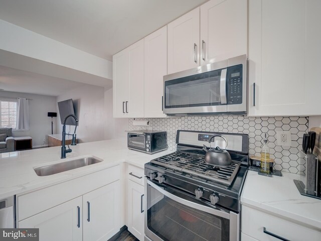 kitchen with stainless steel appliances, decorative backsplash, open floor plan, white cabinets, and a sink