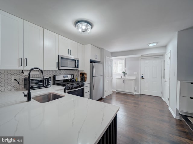 kitchen with decorative backsplash, appliances with stainless steel finishes, white cabinets, a sink, and light stone countertops