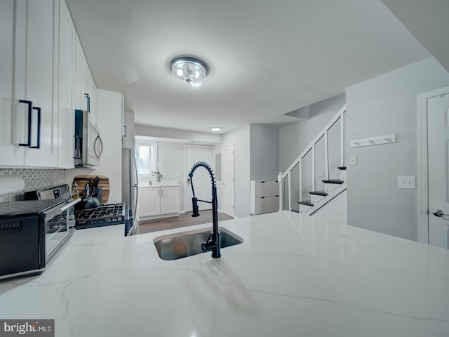 kitchen featuring a toaster, light stone counters, stainless steel appliances, white cabinetry, and a sink