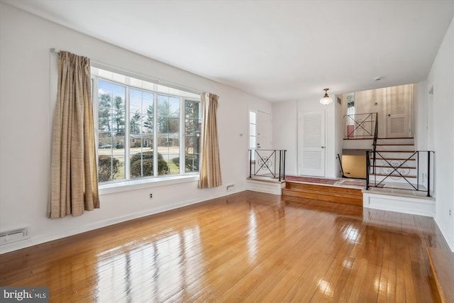 unfurnished living room featuring baseboards, hardwood / wood-style floors, and stairs