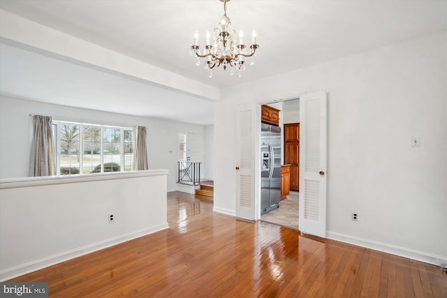 spare room with a notable chandelier, light wood-style flooring, and baseboards