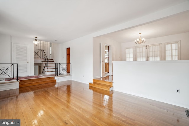 unfurnished living room featuring a chandelier, stairway, and wood-type flooring