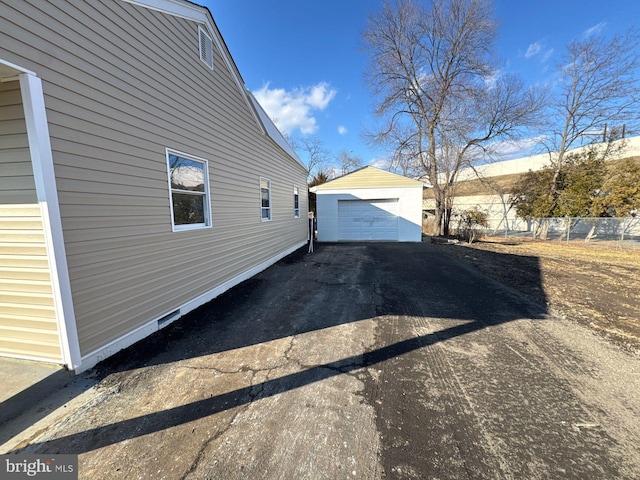 view of property exterior with aphalt driveway, an outbuilding, fence, and a garage