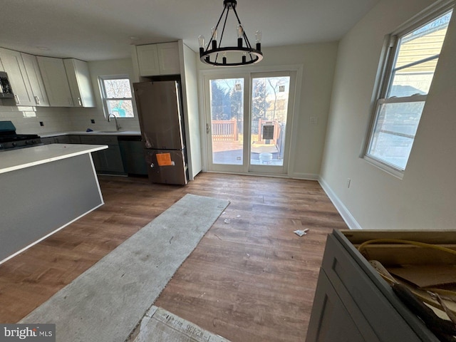 kitchen featuring stainless steel appliances, backsplash, white cabinetry, a sink, and wood finished floors