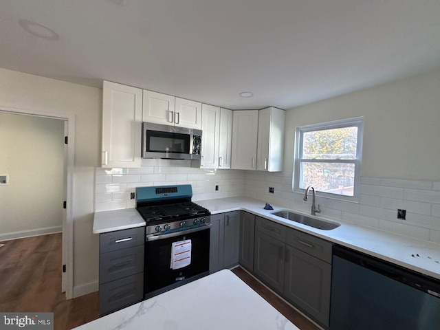 kitchen with dark wood-style flooring, a sink, white cabinets, appliances with stainless steel finishes, and decorative backsplash