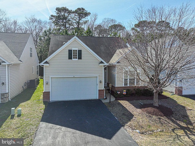 traditional home featuring aphalt driveway, a front yard, brick siding, and central air condition unit