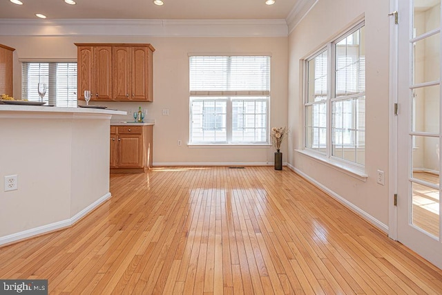 kitchen with light wood-type flooring, brown cabinetry, crown molding, and light countertops