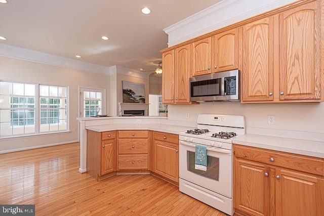 kitchen with crown molding, gas range gas stove, light countertops, stainless steel microwave, and light wood-style floors