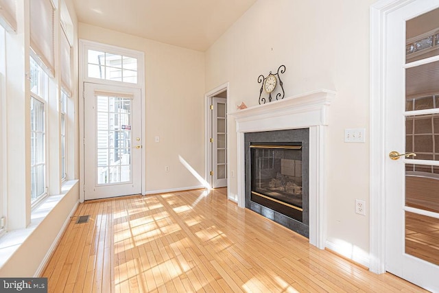 unfurnished living room with wood-type flooring, a glass covered fireplace, visible vents, and baseboards