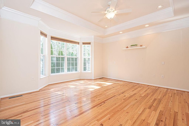 empty room with a tray ceiling, light wood-type flooring, visible vents, and baseboards