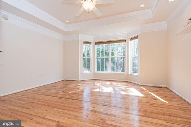 empty room with a tray ceiling, crown molding, recessed lighting, light wood-style floors, and baseboards