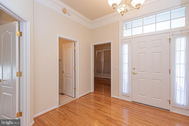 foyer entrance with baseboards, a notable chandelier, crown molding, and light wood finished floors