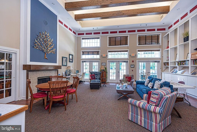 carpeted living area with a fireplace, a high ceiling, beamed ceiling, and french doors