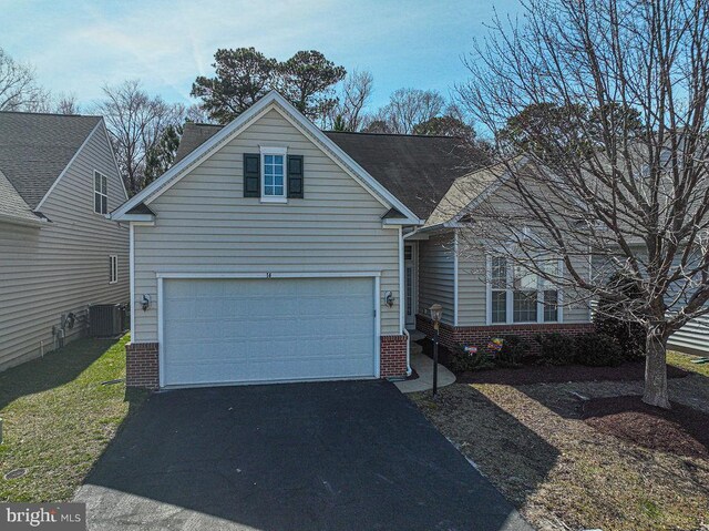 traditional-style house featuring a garage, central air condition unit, aphalt driveway, and brick siding