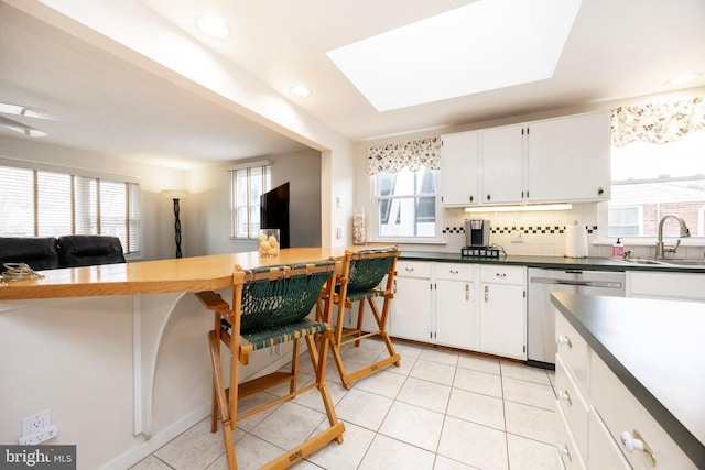 kitchen featuring light tile patterned floors, tasteful backsplash, dark countertops, stainless steel dishwasher, and a sink