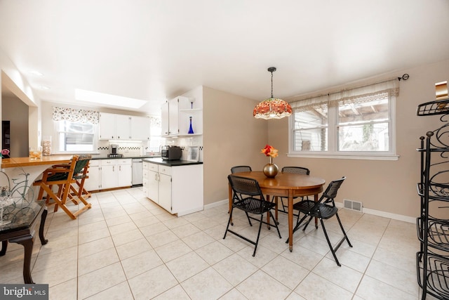 dining space with a skylight, baseboards, visible vents, and light tile patterned flooring