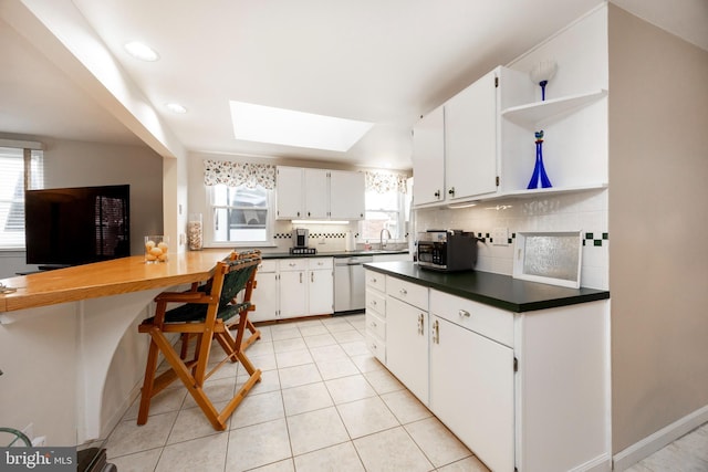 kitchen with a skylight, stainless steel dishwasher, open shelves, tasteful backsplash, and dark countertops