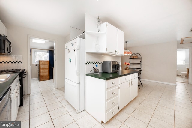 kitchen with black microwave, light tile patterned floors, stainless steel dishwasher, freestanding refrigerator, and dark countertops