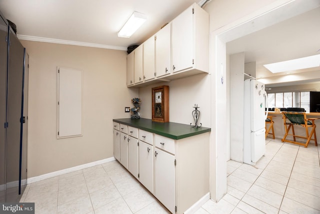 kitchen with a skylight, light tile patterned floors, dark countertops, freestanding refrigerator, and crown molding