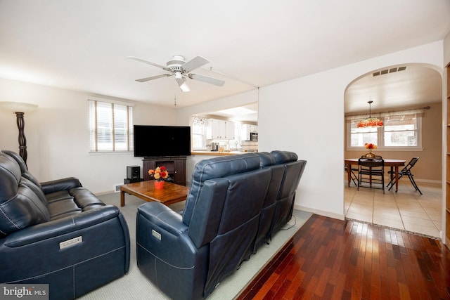 living area featuring arched walkways, visible vents, a ceiling fan, wood finished floors, and baseboards