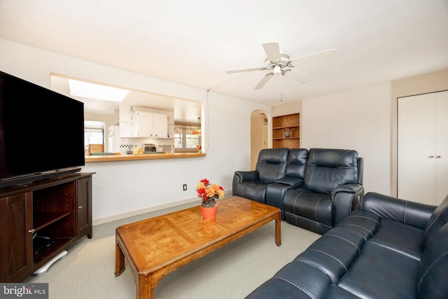 living room with arched walkways, ceiling fan, built in shelves, and light carpet