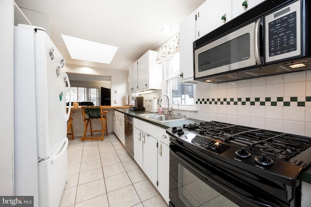 kitchen featuring freestanding refrigerator, light tile patterned flooring, black gas stove, a sink, and dishwasher