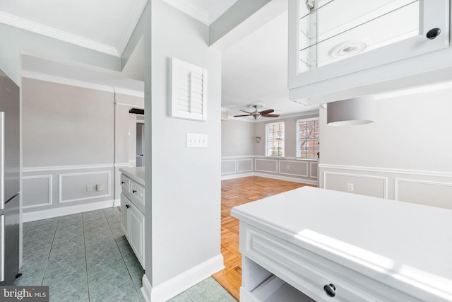 bathroom featuring a ceiling fan, a wainscoted wall, crown molding, a decorative wall, and tile patterned floors