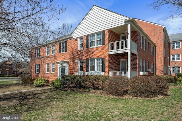 view of front of house with brick siding, a balcony, and a front yard