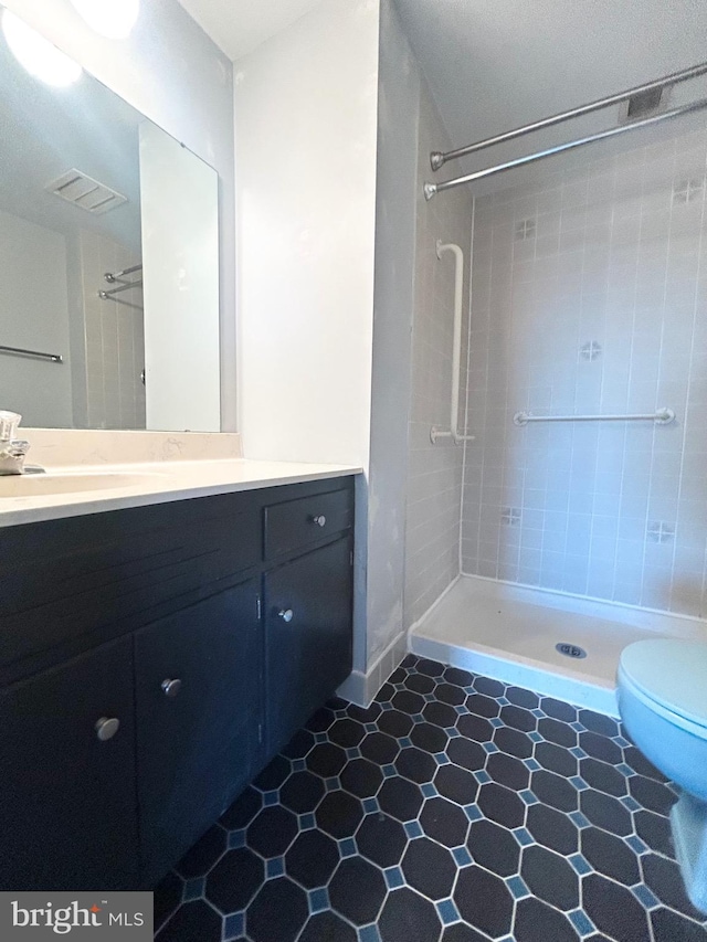 bathroom featuring toilet, visible vents, a tile shower, and vanity