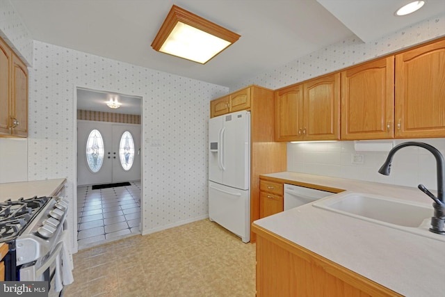 kitchen with a sink, white appliances, light countertops, and wallpapered walls