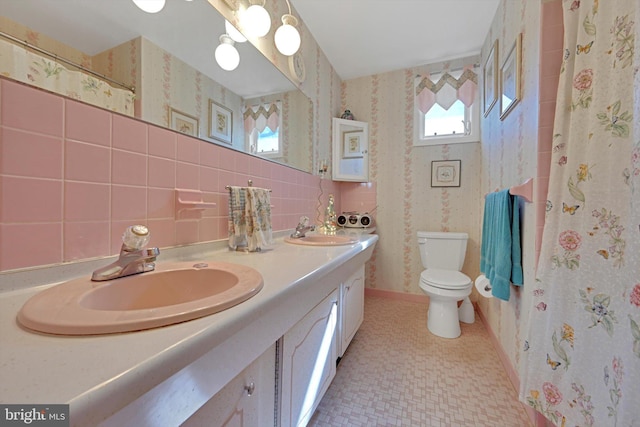 full bath with double vanity, toilet, wallpapered walls, and a sink