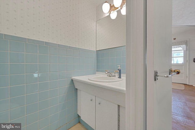 bathroom featuring wallpapered walls, tile walls, vanity, and a wainscoted wall