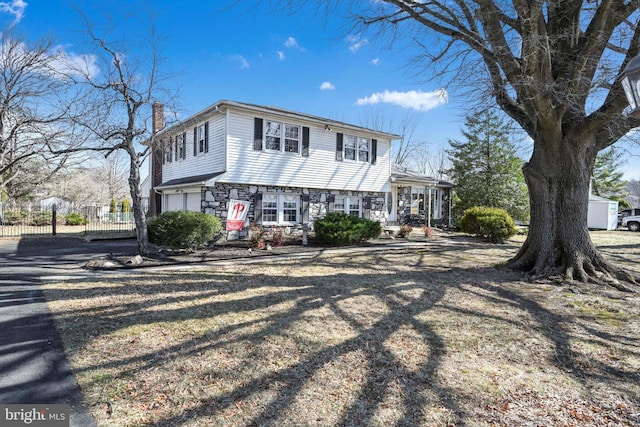 view of front of home featuring an attached garage, fence, stone siding, and a chimney