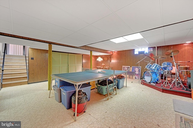 rec room featuring tile patterned floors, wooden walls, and a drop ceiling