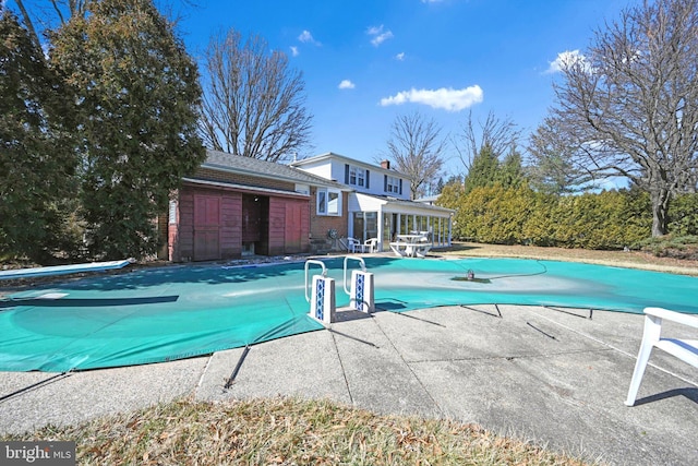 view of swimming pool featuring a covered pool, a patio area, and a diving board