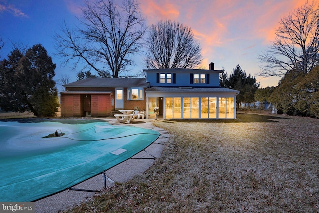 back of property at dusk featuring a covered pool, a patio area, a sunroom, and a chimney