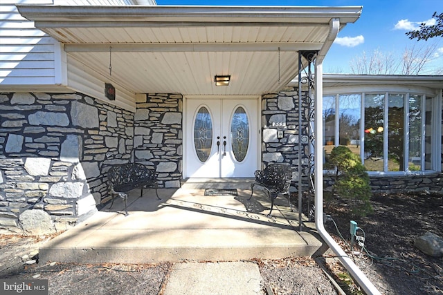 doorway to property featuring a porch, french doors, and stone siding