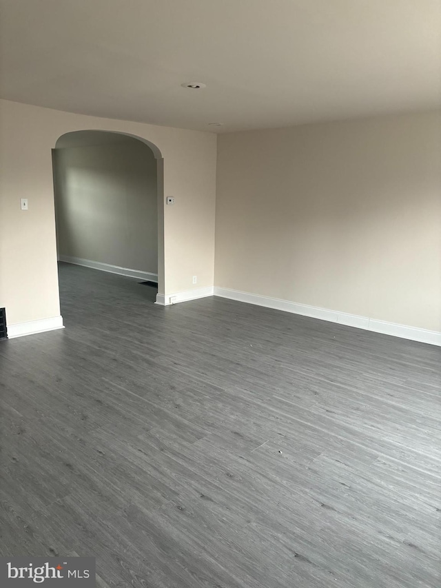 empty room with baseboards, arched walkways, and dark wood-style flooring