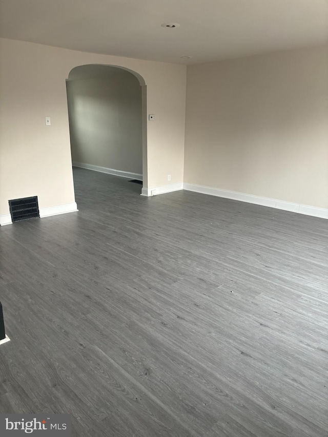 empty room with dark wood-style floors, arched walkways, visible vents, and baseboards