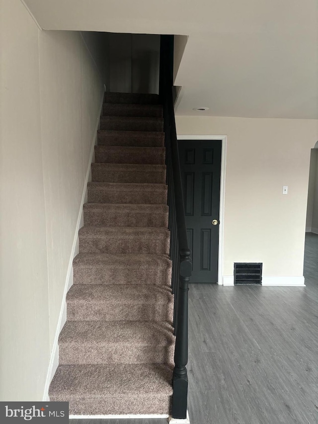 stairway featuring wood finished floors, visible vents, and baseboards