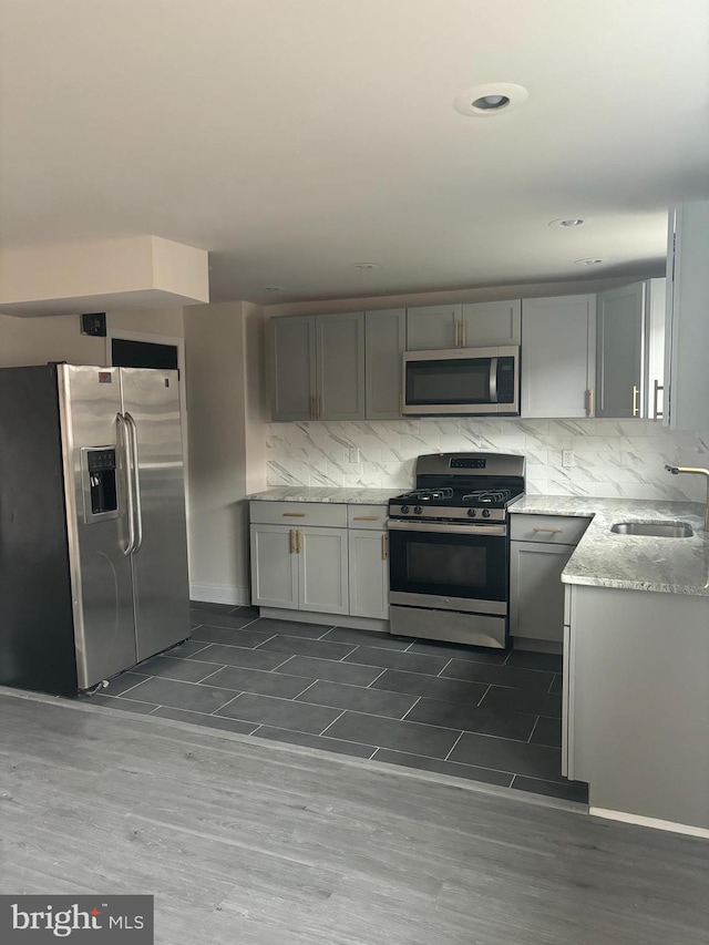 kitchen featuring light stone counters, stainless steel appliances, gray cabinets, decorative backsplash, and a sink