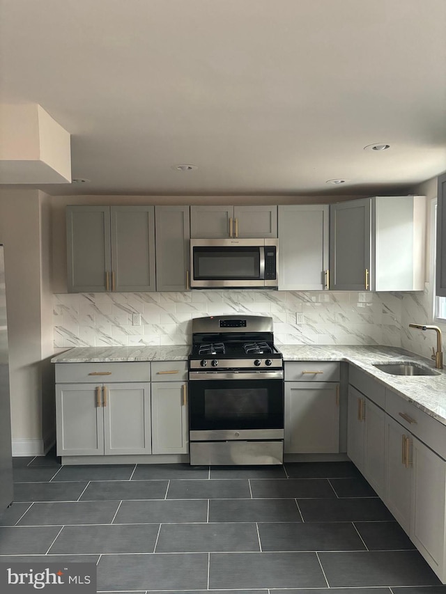 kitchen with stainless steel appliances, gray cabinetry, a sink, and decorative backsplash