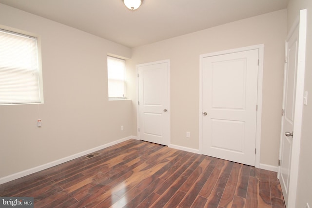 unfurnished bedroom featuring baseboards, visible vents, and dark wood-style flooring